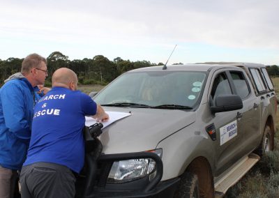 Search and Rescue team studying a map on the bonnet of a car